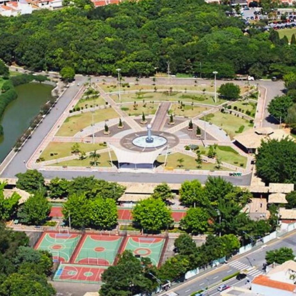 Vista aérea do Parque Espaço Chico Mendes, uma área verde e recreativa localizada em frente ao Trampô Space Coworking, apresentando um design simétrico com caminhos que convergem para um ponto central, quadras esportivas e um lago, oferecendo um local perfeito para pausas relaxantes e inspiradoras para os membros do coworking.