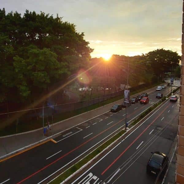 Cena de um pôr do sol deslumbrante capturado em frente ao Trampô Space Coworking, destacando a bela avenida arborizada que serve como ponto de acesso ao espaço de trabalho inovador.