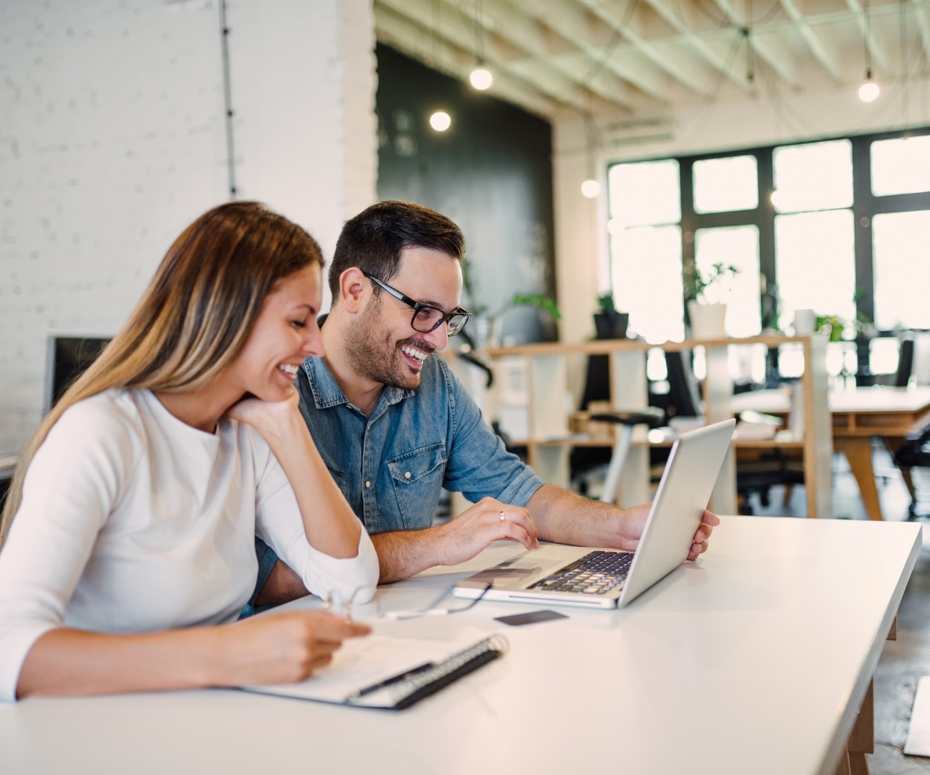 Dois profissionais engajados em networking produtivo no espaço luminoso e moderno, compartilhando ideias e colaborando em um projeto com um laptop, em um ambiente que favorece o crescimento coletivo e a troca de conhecimento.